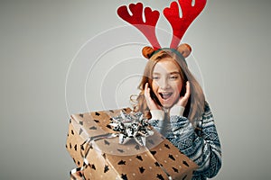 Girl with deer horns in a sweater smiles. She is shocked by such a great gift. Parents pleasantly surprised the teenager