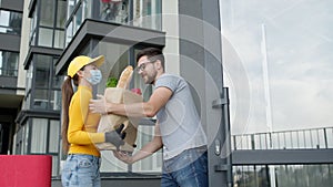 Girl Delivery Service Worker Brings Groceries. She Is Met By Young Man And Takes Package. In Package Are Bread And Salad