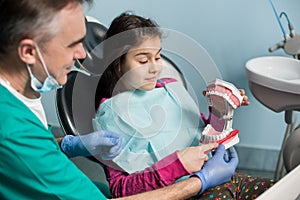 Girl in dentist chair sitting with her pediatric dentist, showing proper tooth-brushing