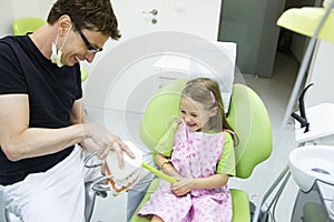 Girl in dentists chair tooth-brushing a model