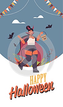 Girl in devil costume holding bucket with pumpkin happy halloween party celebration concept