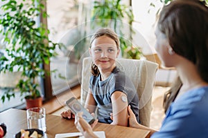 Girl with diabetes checking blood glucose level at home using continuous glucose monitor. Girl& x27;s mother connects CGM