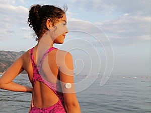 Girl with diabetes is standing on the seashore. On right arm is  white sensor for CGM device. Copy space on right side photo