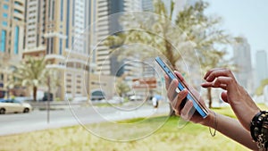 The girl dials a number or message on the smartphone against the backdrop of the city streets of Dubai. Hands close-up.