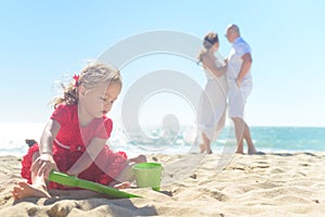 Girl digging sand on beach with parents in background