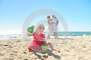 Girl digging sand on beach with parents in background