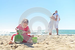 Girl digging sand on beach with parents in background