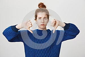 Girl disagree and shows her condemn. Studio shot of displeased frowning redhead european girl in bun and winter sweater