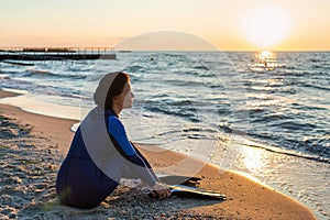 Girl diver in wetsuit puts on flippers sitting on the beach