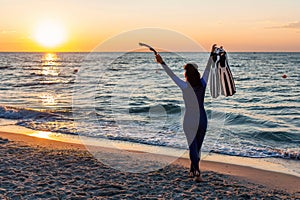 Girl diver in wetsuit throws up her arms to welcome the sunrise