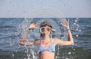 Girl in diving mask plays by spraying sea water