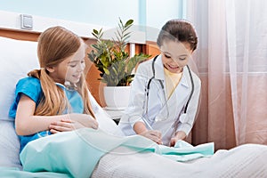 Girl doctor with stethoscope and little patient looking at medical document