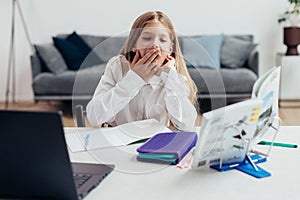 Girl does her homework at home and yawns. She is sleep-deprived or tired and bored