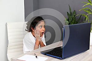Girl does home schooling takes online classes at home on a desk with a laptop, studies, is surprised and participates in class