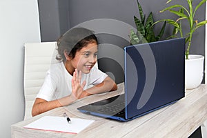 Girl does home schooling takes online classes at home on a desk with a laptop, studies, is surprised and participates in class