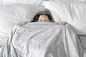 The girl does not want to get out of bed in the morning. Hiding in a blanket. View from above. Ambush in bed