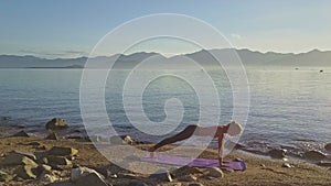 Girl Does Yoga Exercise on Ocean Coast against Distant Hills