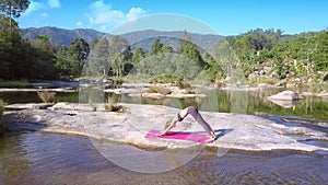 Girl does yoga on flat stone among pictorial river