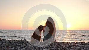 Girl and dog gaze over the sea at sunset, serene companionship