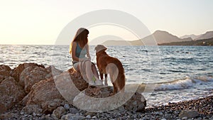 Girl and dog gaze over the sea at sunset, serene companionship