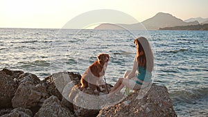 Girl and dog gaze over the sea at sunset, serene companionship
