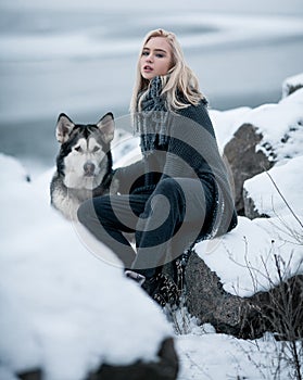Girl with dog Malamute among rocks in winter.