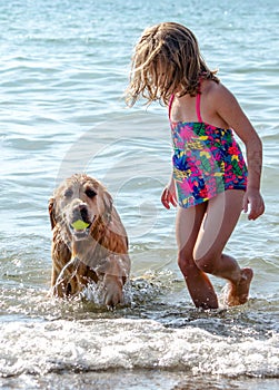 Girl and dog playing with a ball at the beach