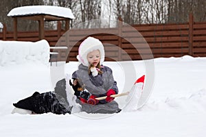 Girl and dog playing in snow with a shovel