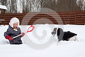 Girl and dog playing in snow with a shovel