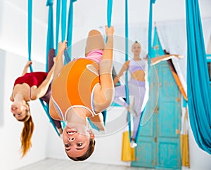 Girl doing aerial yoga asana on one leg with back arched in hanging hammock