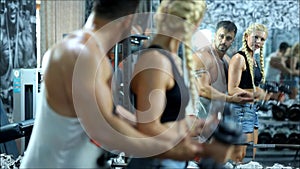 The girl doing exercices with a heavy load with gym equpment by supporting the men behind