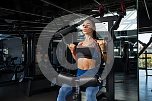 Girl doing exercises for back muscles on strength machines at gym