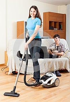 Girl doing floor cleaning while man resting over sofa