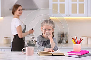 Girl doing homework while mother cooking in kitchen