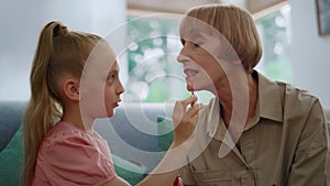 Girl doing makeup for grandmother. Woman and granddaughter playing with lipstick