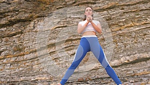 Girl doing squat lunge the bodyflex during breathing exercises on the rock background.