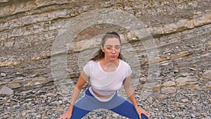 Girl doing squats the bodyflex during breathing exercises on the rock background.