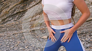 Girl doing squats the bodyflex during breathing exercises on the rock background. Close-up belly and body