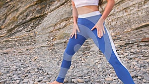 Girl doing squats the bodyflex during breathing exercises on the rock background. Close-up belly and body