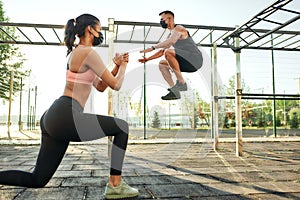 Girl doing squats while man jumping on urban sport ground