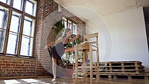 Girl doing stretching at the ballroom. Attractive girl in black tutu is engaged in ballet. Gymnast girl doing warm-up