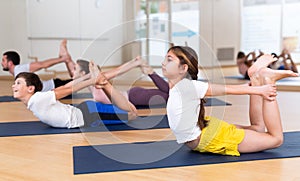 Girl doing stretching in Dhanurasana pose while exercising yoga with family in studio