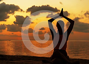 Girl doing yoga on the beach at sunset