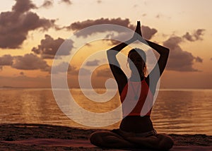 Girl doing yoga on the beach at sunset