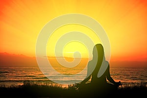 Girl doing yoga meditating in the beach sitting on the grass at sunset. Empty copy space