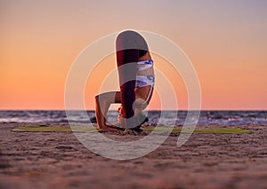 Girl doing yoga by the sea at sunset