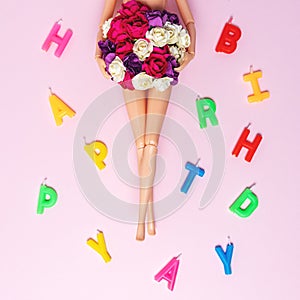 Girl doll with colorful flowers and birthday candles on pink background. Creative minimal holiday concept