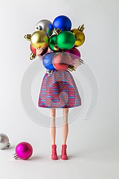 Girl doll holding colorful baubles and preparing for Christmas home decoration minimal creative holiday concept