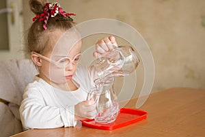 Girl with Down syndrome gently pours water from a jug into a jug