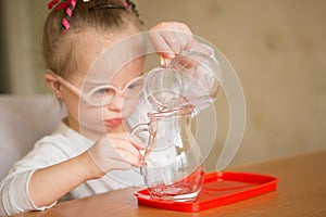 Girl with Down syndrome gently pours water from a jug into a jug